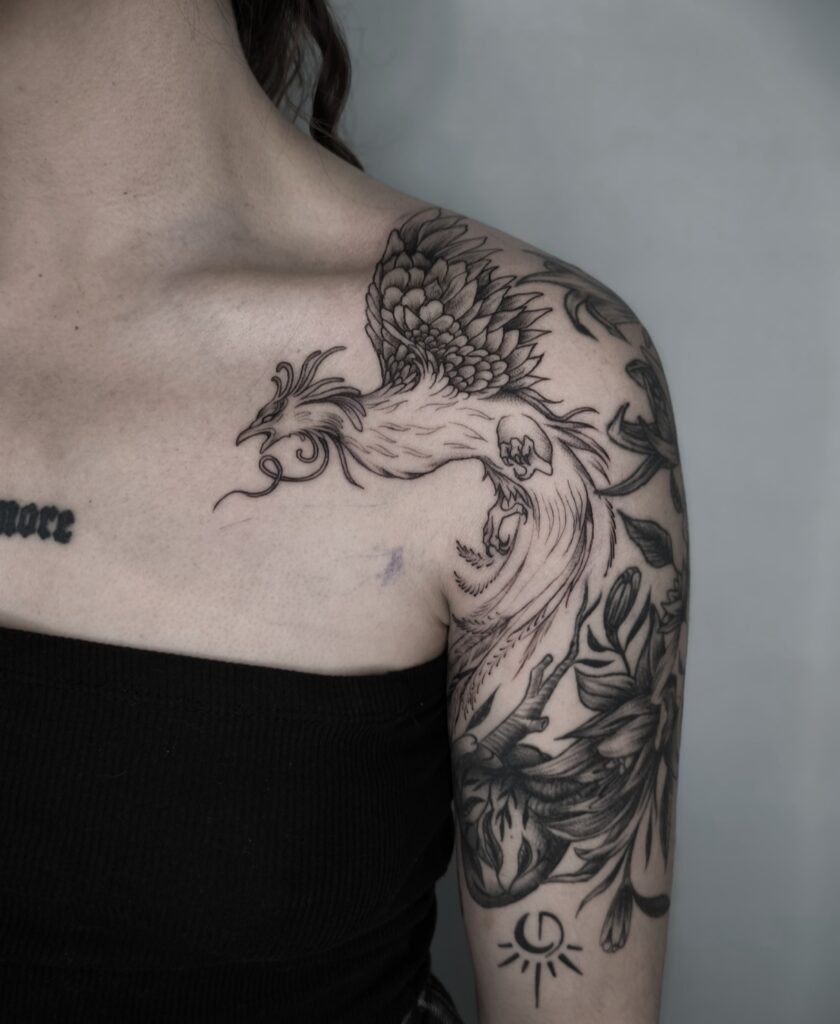 Tatuaje de fénix en negro sobre hombro y brazo