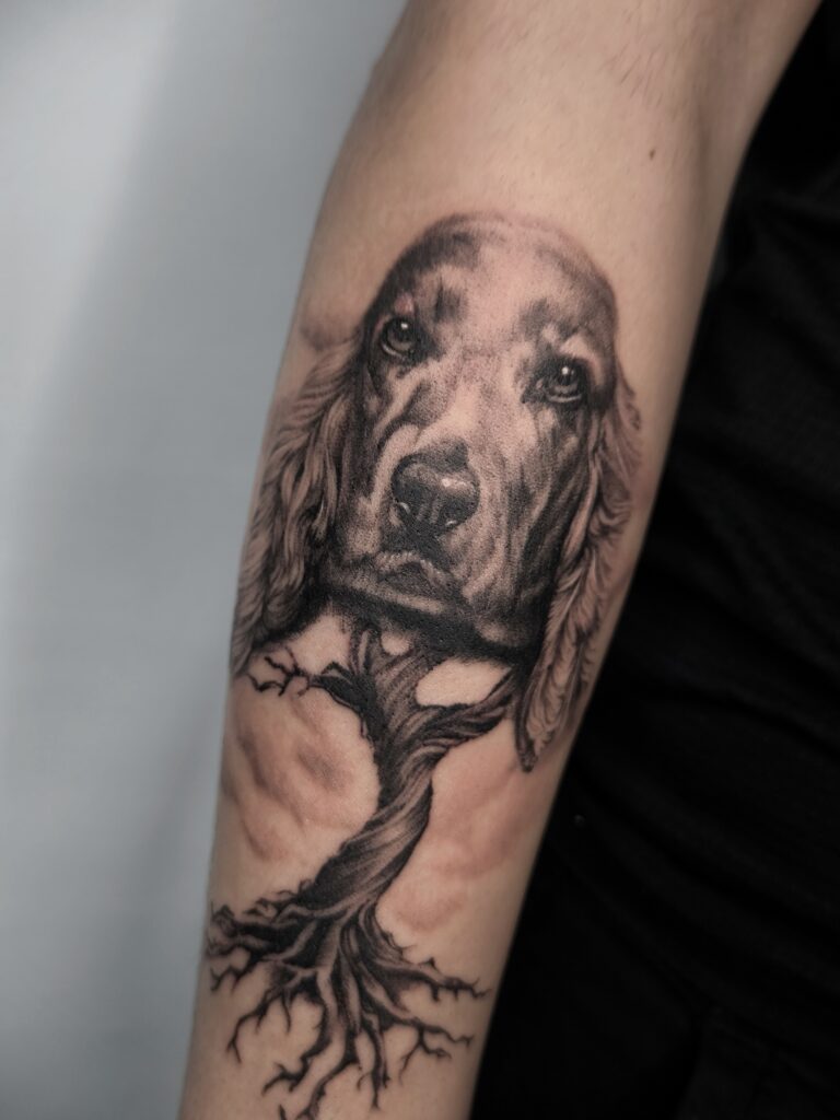Tatuaje realista de perro y árbol en antebrazo en Bilbao