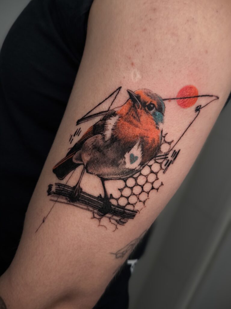 Tatuaje de pájaro a color con elementos geométricos en el brazo en Bilbao