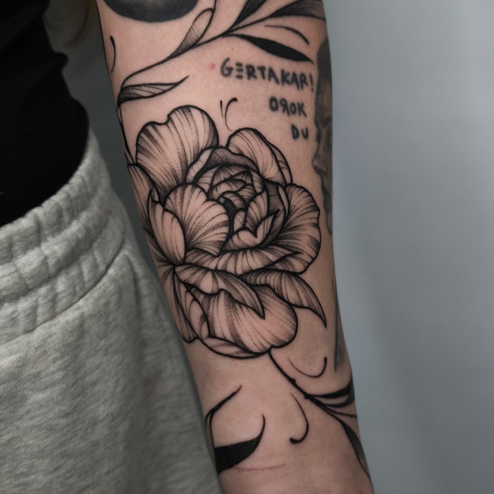 Tatuaje de peonía con lettering en antebrazo en Bilbao